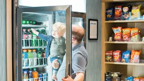 Ein Mann hält ein Kind vor einem Kühlschrank, der mit Getränken und Snacks gefüllt ist.