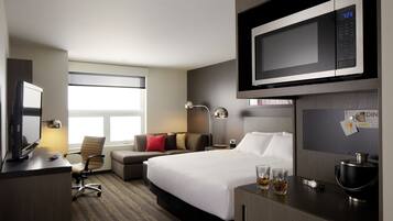 A hotel room with a bed, a desk with a computer, a microwave, a coffee maker, and a window with a view.