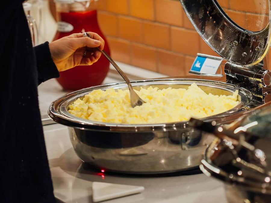 A buffet setup with a large metal bowl of mashed potatoes.