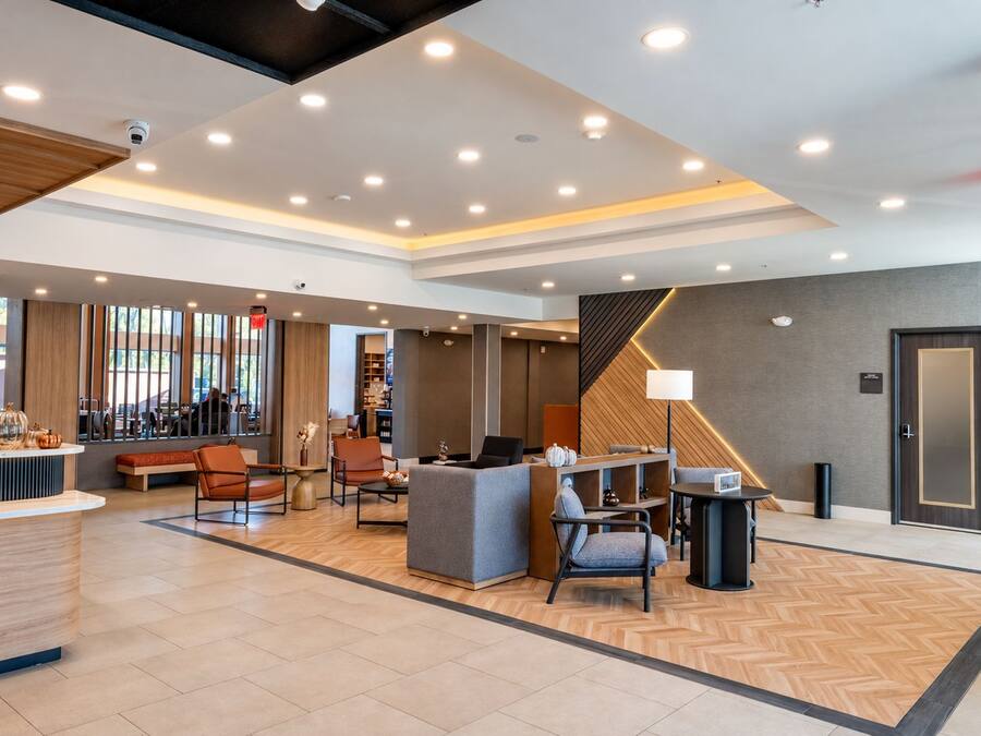 A modern hotel lobby with a reception desk, seating area, and a staircase leading to upper floors.