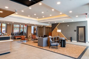 Un moderno vestíbulo de hotel con mostrador de recepción, zona de estar y una escalera que conduce a los pisos superiores.