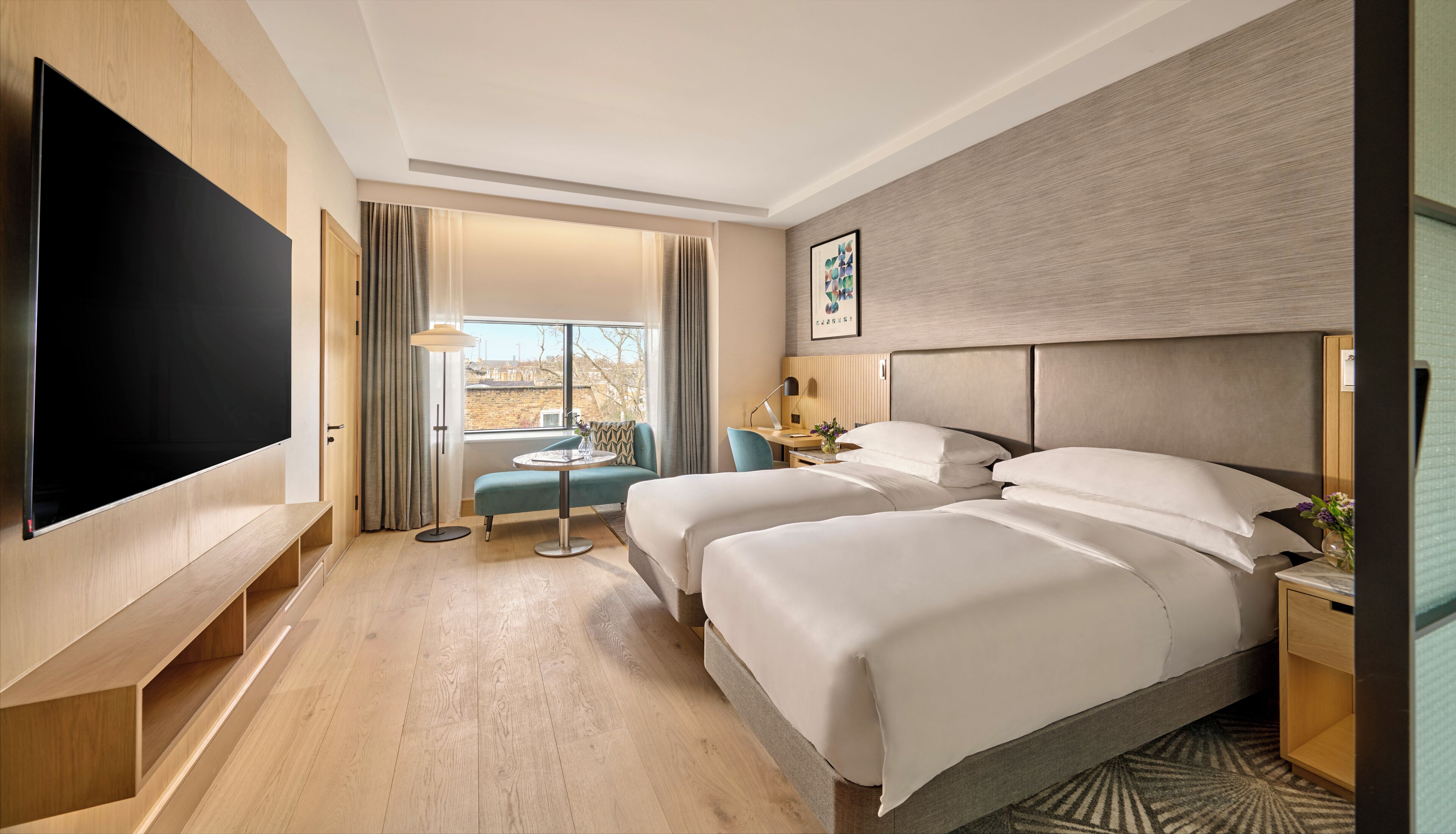 Ein Hotelzimmer mit großem Flachbildfernseher, zwei Betten, einem kleinen Tisch und einem Sessel.