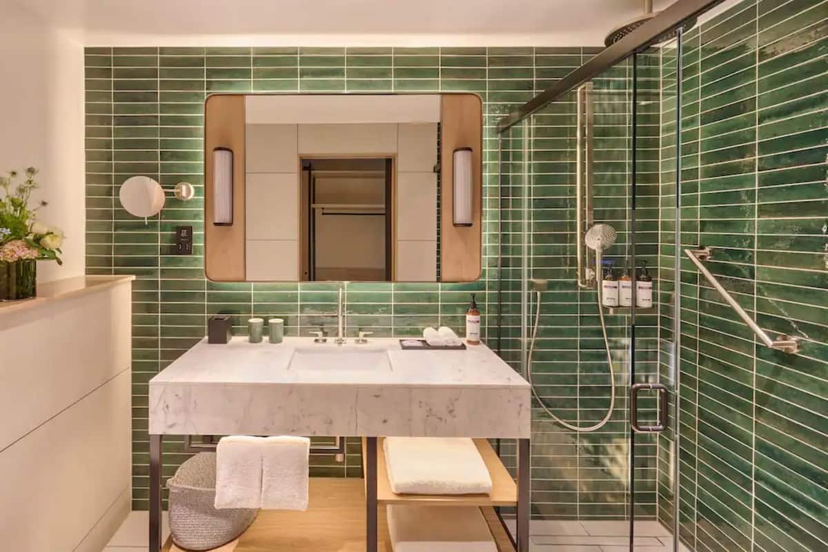 A modern bathroom with a large mirror, a sink with two basins, a shower, and a bench.