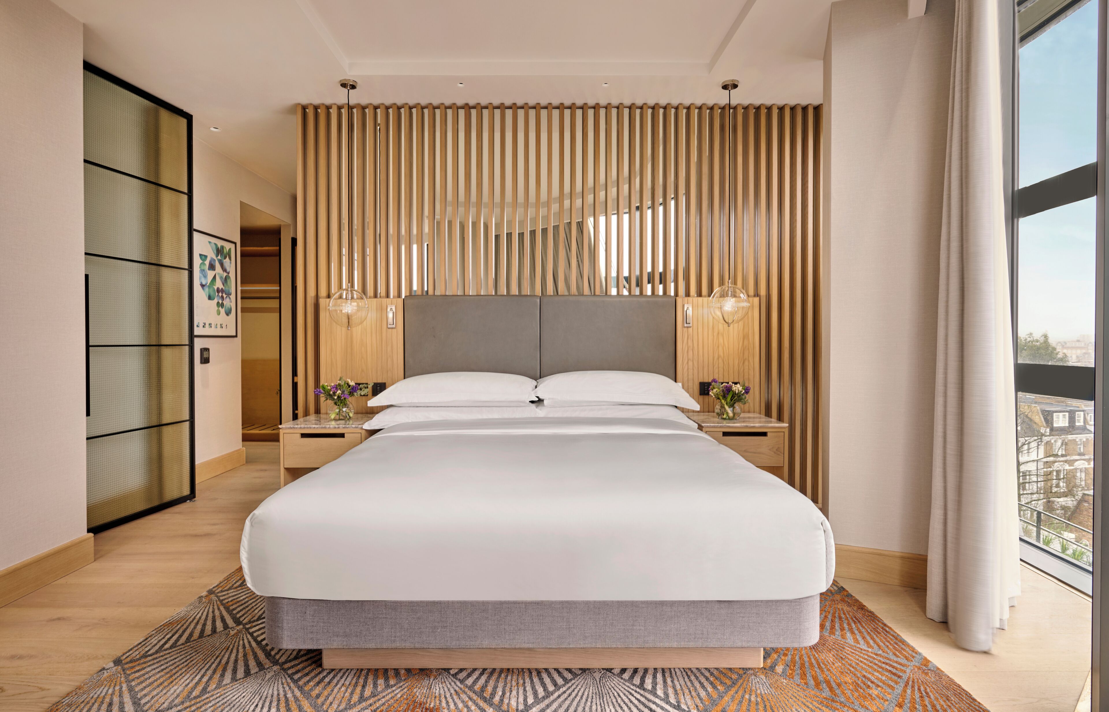 Una habitación de hotel moderna con una cama grande, paneles de madera y vistas a la ciudad.