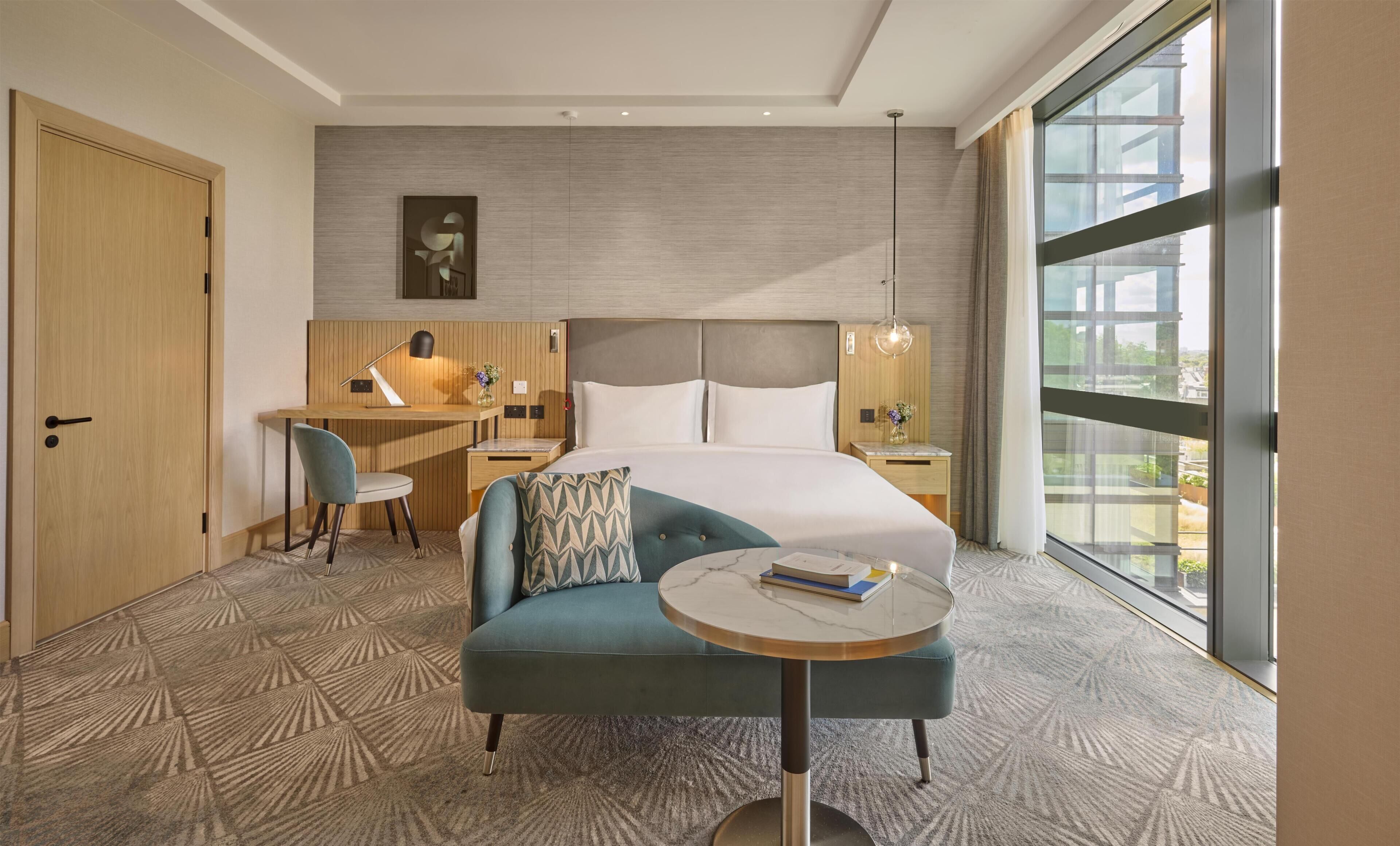 A hotel room with a bed, a desk, a chair, a round table, and a large window.