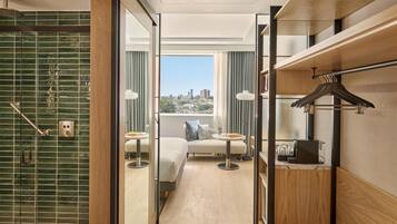 A hotel room with a shower, a bed, a seating area, and a view of the city.