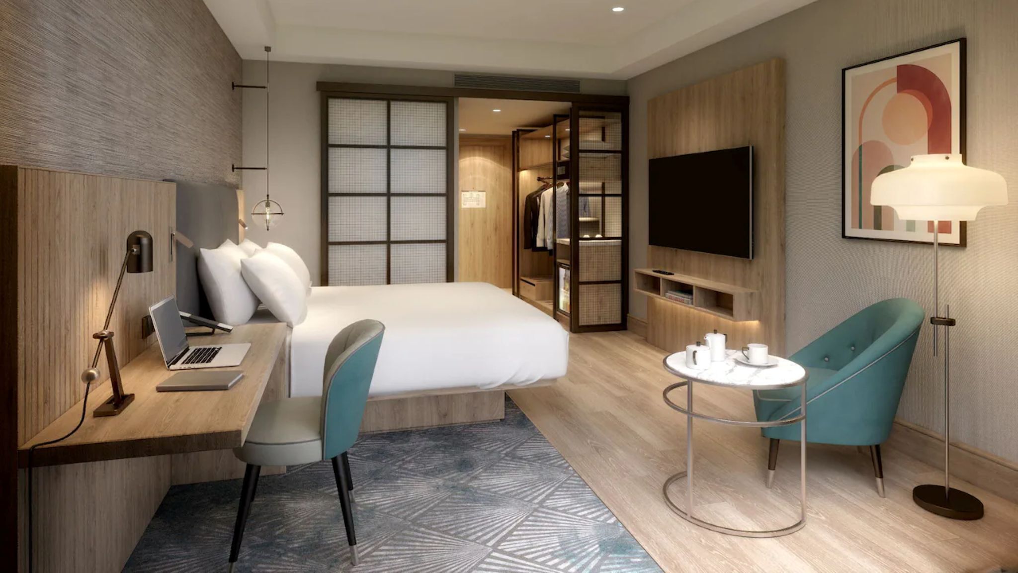A modern hotel room with a bed, desk, chair, TV, and a small round table with a lamp.
