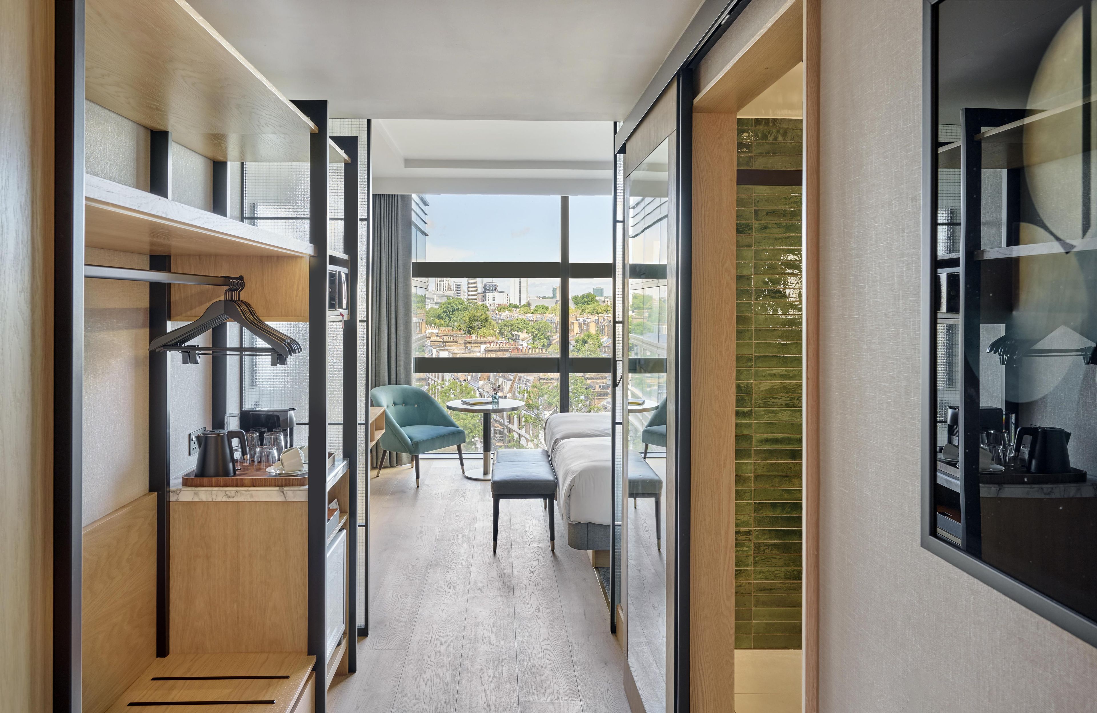 A modern hotel room with a balcony, a seating area, and a view of the cityscape.
