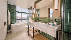 A modern bathroom with a freestanding bathtub, a large mirror, and a vanity with a sink and towel rack. - Hyatt Regency London Olympia (London)