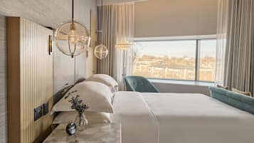 A hotel room with a large bed, a desk with a vase of flowers, a clock, and a view of the city through the window.
