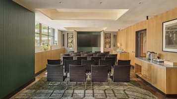 Uma sala de conferências com tela grande, diversas cadeiras, painel de parede de madeira e área de recepção com balcão.