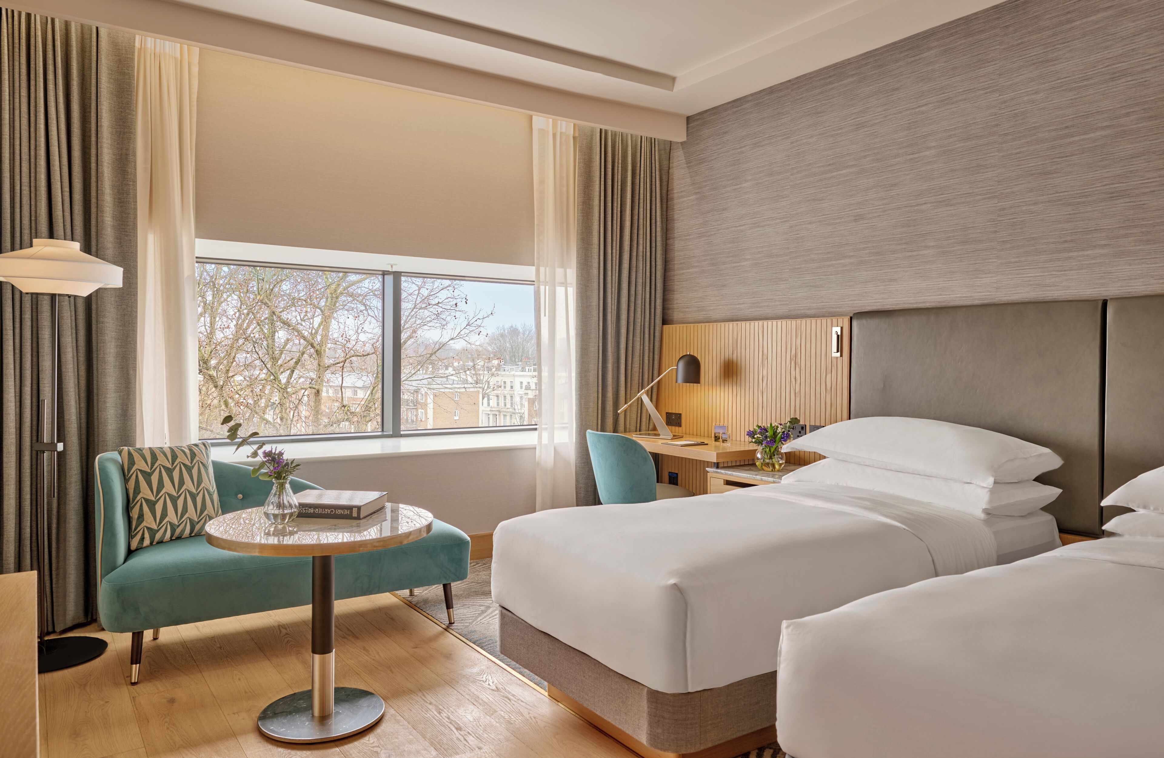 A hotel room with a large window, a sofa, a round table, and two beds.