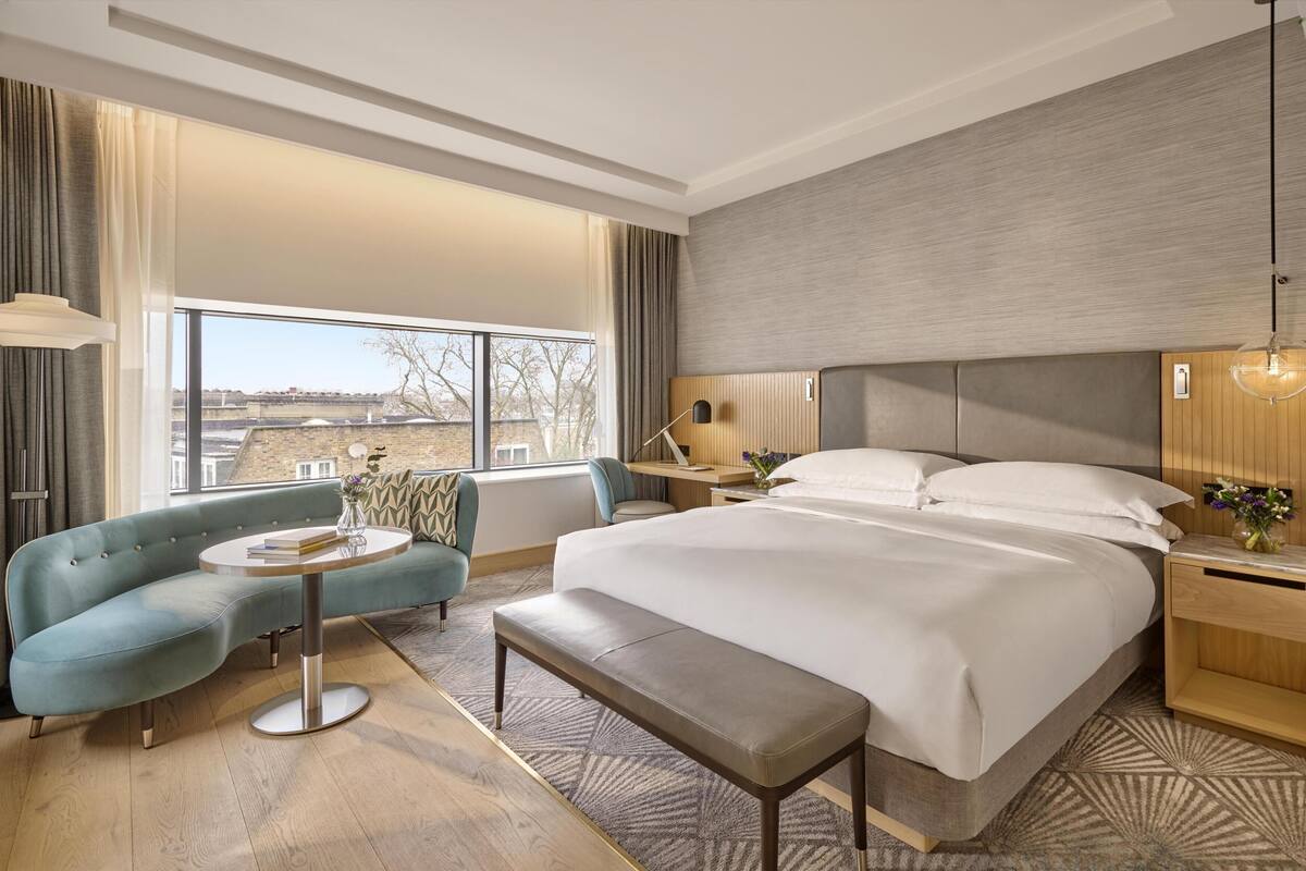 A modern hotel room with a large bed, a sofa, a desk, and a view of the city.