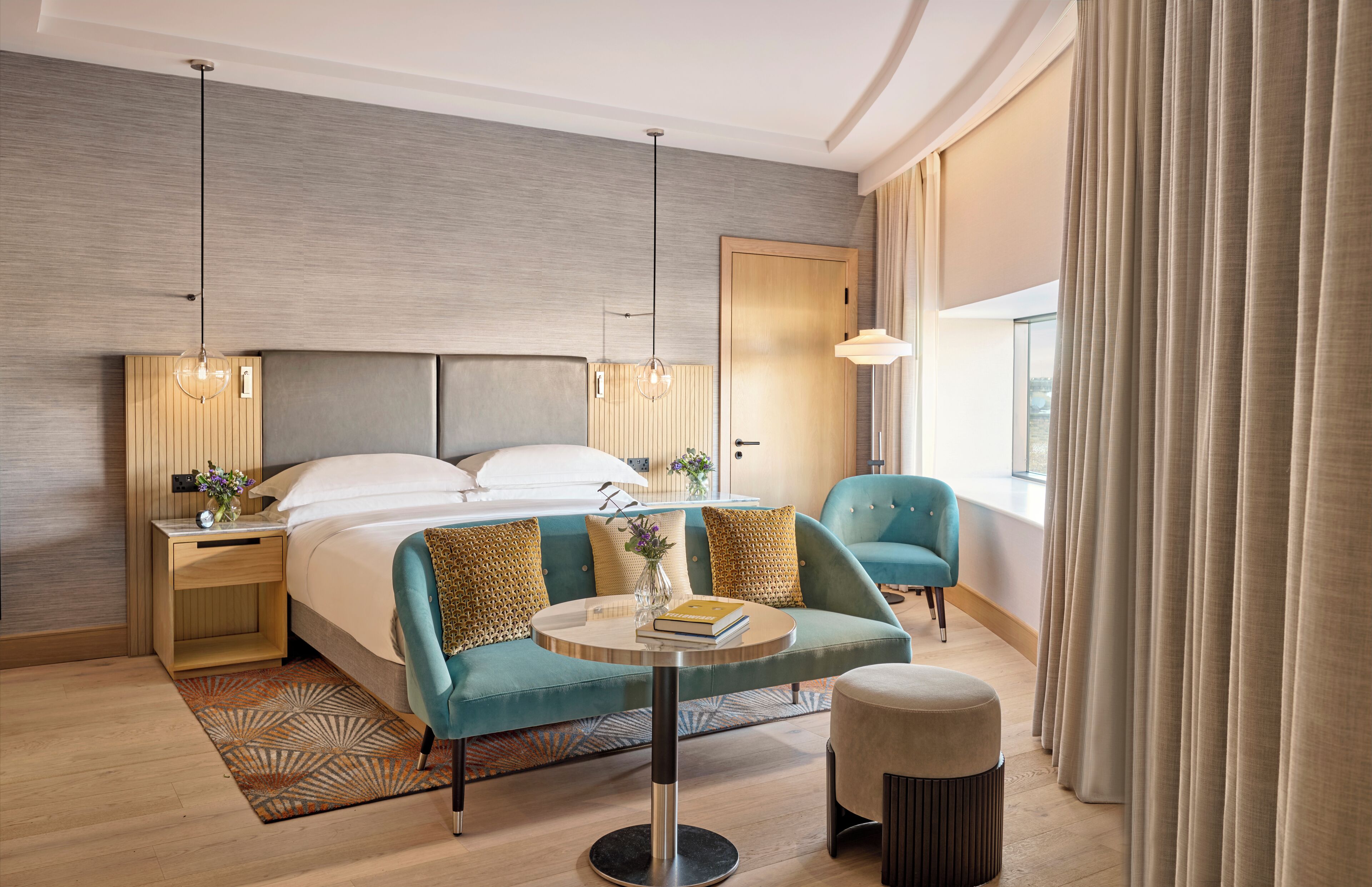 Quarto de hotel moderno com uma cama grande, um sofá, uma mesa redonda e vista para a cidade pela janela.