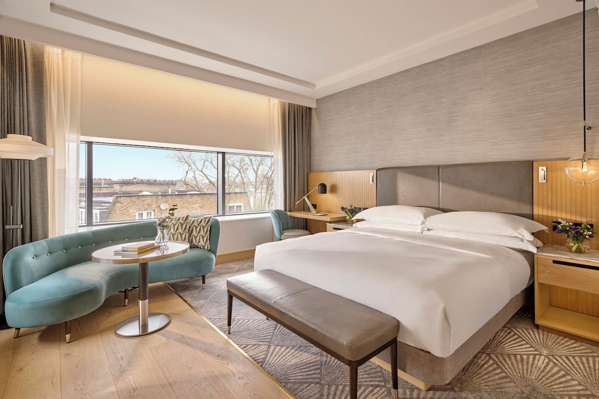 A modern hotel room with a large bed, a sofa, a desk, and a view of the city.