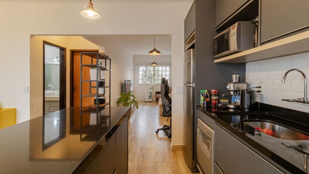 A modern kitchen with a central island, stainless steel appliances, and a view into the living area. - Casa Pet Friendly no Condom nio Bell Park (São José dos Campos)