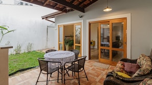 A patio with a round table and chairs, a wicker sofa, and a glass door leading to an indoor area. - Casa Pet Friendly no Condom nio Bell Park (São José dos Campos)