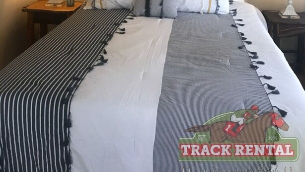A neatly made bed with striped bedding, a welcome sign, a framed picture, and a lamp on a bedside table.