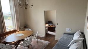 A living room with a wooden dining table, white chairs, a gray sofa, and a chandelier. - Boutique Three Bedroom Apartment (La Porte)