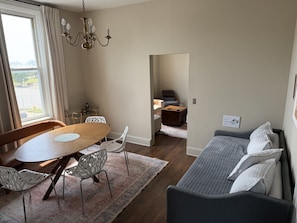 A living room with a wooden dining table, white chairs, a gray sofa, and a chandelier. - Boutique Three Bedroom Apartment (La Porte)