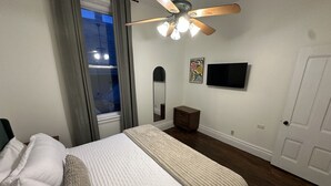 A bedroom with a bed, a ceiling fan, a TV, a mirror, and a door. - Boutique Three Bedroom Apartment (La Porte)