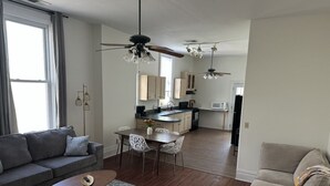 A modern living room with a gray sofa, a coffee table, and a beige armchair. There is a dining area with a table and chairs, and a kitchen in the background. - Boutique Three Bedroom Apartment (La Porte)