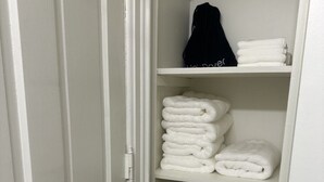 A white closet with shelves holding folded towels and a black bag. - Boutique Three Bedroom Apartment (La Porte)