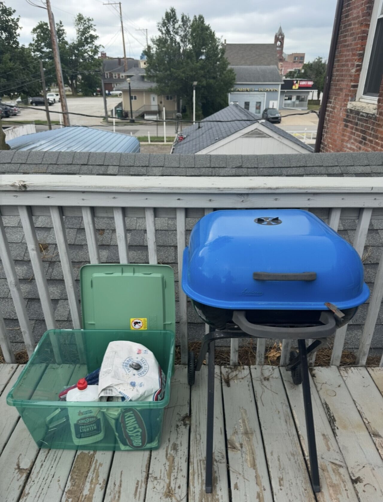 A wooden deck with a barbecue grill and a green storage bin.