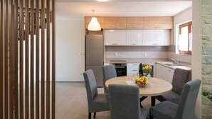 Eine moderne Küche mit weißen Schränken, einem eingebauten Backofen und einem Essbereich mit rundem Tisch und grauen Stühlen.