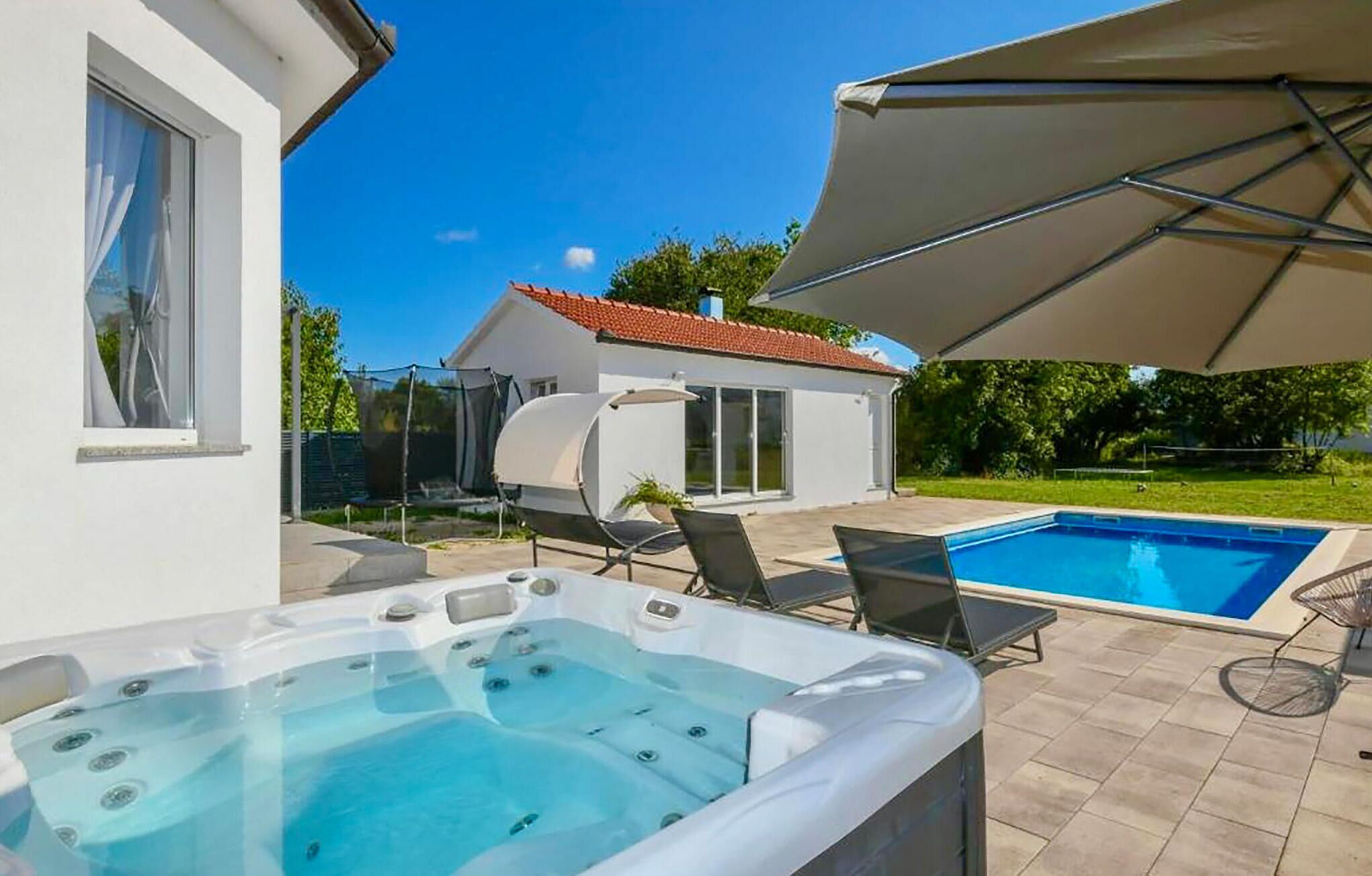 A backyard with a hot tub, a swimming pool, and a covered patio area.