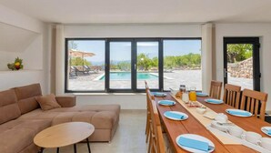 A modern living room with a large window overlooking a pool and outdoor seating. - Gorgeous home in Postranje (Postranje)