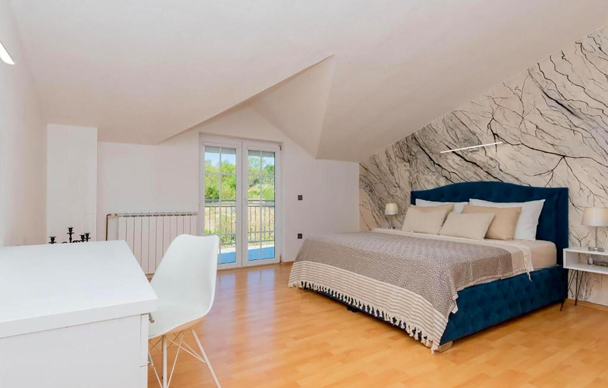 A bedroom with a bed, a desk, and a balcony.