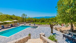 A swimming pool with lounge chairs and umbrellas, surrounded by a stone deck and trees. - Gorgeous home in Postranje (Postranje)