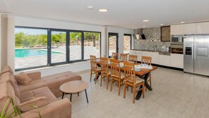 A spacious living room with a large window, a dining area with wooden chairs and a table, and a modern kitchen with stainless steel appliances. - Gorgeous home in Postranje (Postranje)