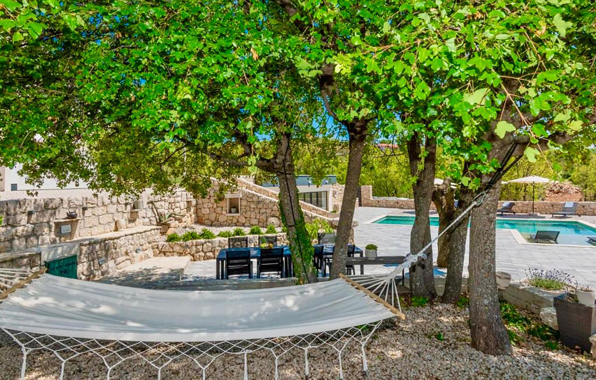 A hammock under a tree, a pool, stone walls, and outdoor furniture.