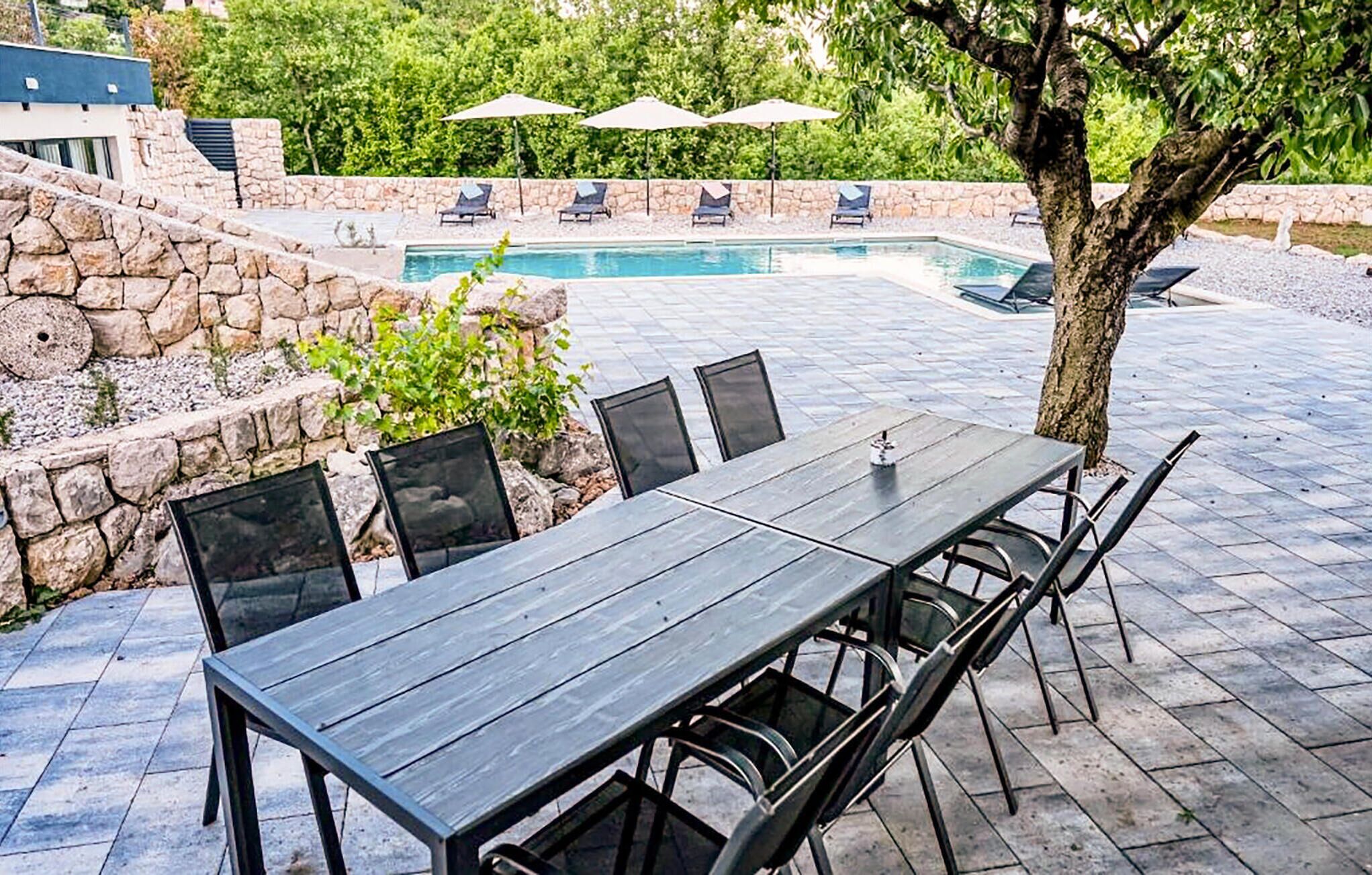 Un patio al aire libre con piscina, muros de piedra y sillones de descanso.