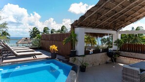 A rooftop pool area with lounge chairs, a thatched roof, and a view of the ocean. - Ocean View Penthouse in the Main Center (Playa del Carmen)