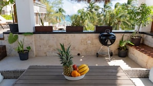 A wooden table with a bowl of fruit on a balcony with potted plants and a view of palm trees. - Ocean View Penthouse in the Main Center (Playa del Carmen)