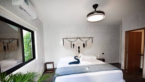 Um quarto moderno com uma cama grande, uma luminária no teto, uma decoração de macramé na parede e uma janela com vista para o verde.