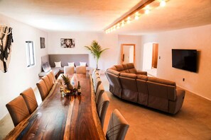 A spacious living room with a large wooden dining table, a sectional sofa, and a flat-screen TV mounted on the wall. - Gran Palapa house  private pool and cenote access (Playa del Carmen)