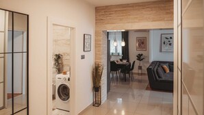 Een moderne woonkamer met een bank, een eethoek met een tafel en stoelen, en een wasruimte met een wasmachine.