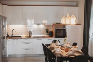 A modern kitchen with white cabinets, a wooden countertop, and a dining area set for a meal. - Apartment LuMary Zadar (Zadar)