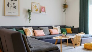 Een moderne woonkamer met een grijze bank, meerdere kussens, een ronde salontafel en een hangplant.