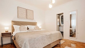 Een slaapkamer met een groot bed, twee nachtkastjes, een spiegel en een deur naar een badkamer.