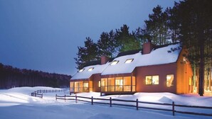 A modern, multi-story wooden house with large windows and a snow-covered roof, surrounded by a wooden fence and trees. - Rustic 2BR Cabin at Christmas Mountain Village – Family Adventure Awaits (Wisconsin Dells)