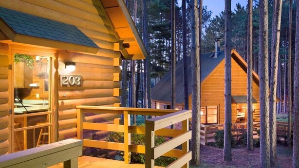 A log cabin with a number '203' on the door, wooden deck, and a forested background. - Rustic 2BR Cabin at Christmas Mountain Village – Family Adventure Awaits (Wisconsin Dells)