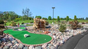 A miniature golf course with a green putting surface, a stone structure, and a wooden fence. - Rustic 2BR Cabin at Christmas Mountain Village – Family Adventure Awaits (Wisconsin Dells)
