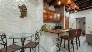 A kitchen with white stone walls, wooden cabinets, a glass table, and bar stools. - Su Lizu, charm and relaxation in the historic center of Cagliari - with patio. (Cagliari)