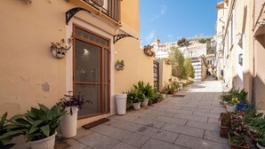 A narrow alleyway with potted plants lining the path, leading to a building with a wooden door and window shutters. - Su Lizu, charm and relaxation in the historic center of Cagliari - with patio. (Cagliari)