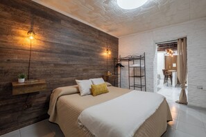 A modern bedroom with a wooden wall, a bed with a white and beige bedspread, a hanging light fixture, and a small plant on a shelf. - Su Lizu: Charm and relaxation in the historic center of Cagliari—with a patio. (Cagliari)